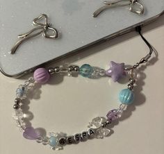 two bracelets with charms on them sitting next to a cell phone and silver scissors