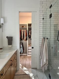 a walk in shower sitting next to a white sink and wooden cabinets under a mirror