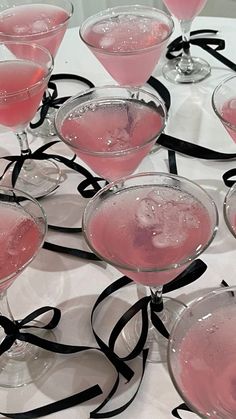 several martini glasses with pink liquid in them sitting on a white tablecloth covered table