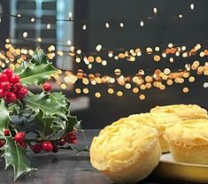 two muffins sitting on a plate next to a holly bush and christmas lights