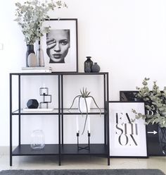 a black and white shelf with vases, plants and pictures on it's sides