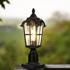 an old fashioned street light on top of a wooden fence with trees in the background