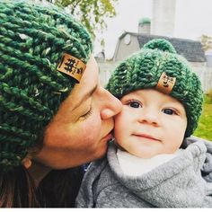 a woman kissing a baby wearing a green knitted hat with wooden crosses on it