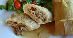 an enchilada with meat and vegetables on a white plate next to lettuce