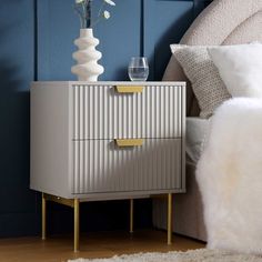 a bed with a white and gold nightstand next to a blue wall