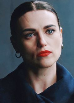 a woman with blue eyes and red lipstick looks at the camera while wearing large earrings