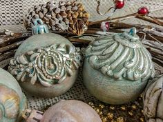 three ornaments sitting on top of a table next to a pine cone and some twigs