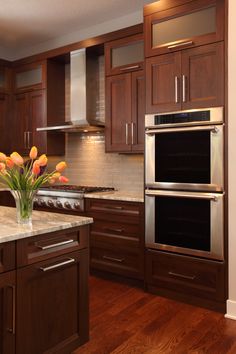 a kitchen with wooden cabinets and marble counter tops, two ovens and an island