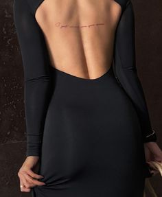 the back of a woman's black dress with writing on her left shoulder and right arm