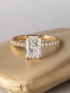 a cushion cut diamond ring on top of a gold pillow