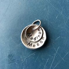 two personalized charms sitting on top of a blue surface with the word made in metal