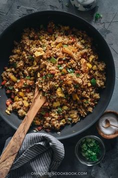 a pan filled with rice and vegetables on top of a table next to a wooden spoon