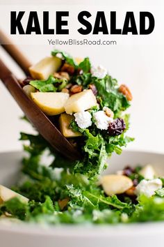 kale salad with apples and feta cheese in a white bowl on a wooden spoon