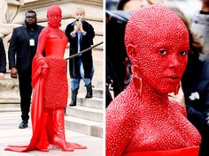 a woman dressed in red poses for the camera and people are taking pictures behind her