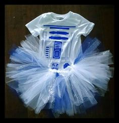 a white shirt and blue tutu with a star wars design on the front, sitting on a wooden floor