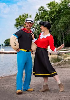 a man and woman dressed in costumes standing next to each other on the beach near water