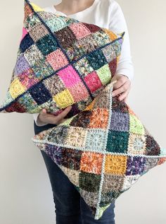 a woman holding a multicolored crocheted pillow