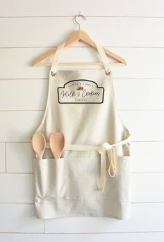 two wooden spoons are in the pocket of an apron hanging on a white wall