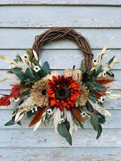 a wreath with dried flowers and leaves hanging on a wooden wall next to a door