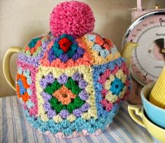 a colorful crocheted tea pot sitting on top of a table next to a bowl