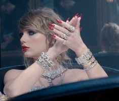 a woman with red nail polish holding her hand up to her face while sitting in a car