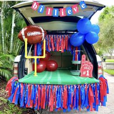 an open trunk with balloons, streamers and footballs on the tailgate for a birthday party