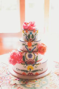 a three tiered cake decorated with flowers on top of a table next to a window