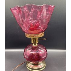 a pink glass vase sitting on top of a metal stand with a cord attached to it