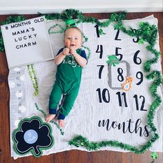 a baby laying on top of a blanket next to a clock and shamrocks decoration