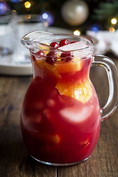 a pitcher filled with liquid sitting on top of a wooden table next to a christmas tree