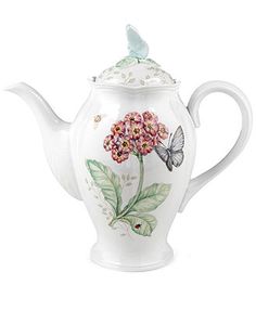 a white tea pot with flowers and butterflies on the top, sitting in front of a white background