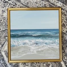 the painting is hanging on the wall by the ocean's edge, and it has waves coming in from the water