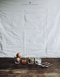 three glasses and spoons sitting on a table next to an egg in the middle