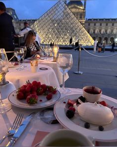 the table is set with plates and bowls of fruit, wine glasses and silverware