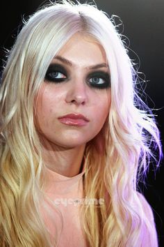 a woman with long blonde hair and blue eyes wearing black make up on her face