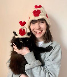 a woman is holding a black cat wearing knitted hearts on it's hats