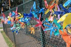 many colorful pinwheels are attached to a chain link fence