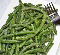 a white plate topped with green beans next to a fork