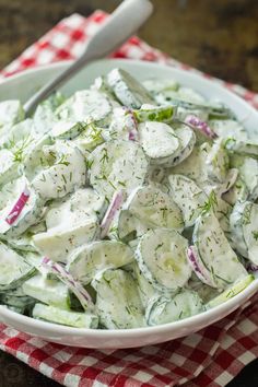 a white bowl filled with cucumber salad on top of a red and white checkered cloth