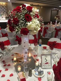 a vase filled with red and white flowers sitting on top of a table covered in candles