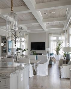 a large open concept living room and dining area with white furniture, chandelier, marble countertops, and exposed wood ceiling