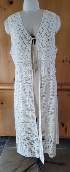 a white crocheted vest is on a mannequin with a wooden wall in the background