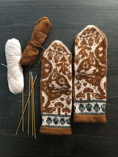 two brown mittens sitting on top of a wooden table next to yarn and knitting needles