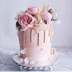 a pink cake with frosting and flowers on top sitting on a marble countertop