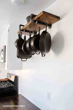 pots and pans are hanging on the wall above an oven in a kitchen with white walls