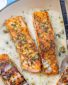 three salmon fillets in a skillet with white sauce