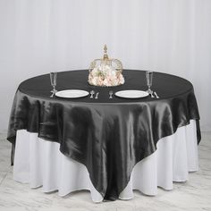 the table is set with two white plates and a black cloth draped over it, along with silverware