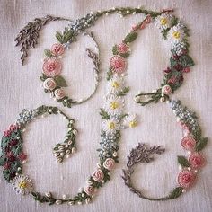 several different types of flowers and leaves on a white table cloth with beads, pins and thread