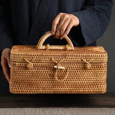 a person holding a wicker suitcase on top of a table