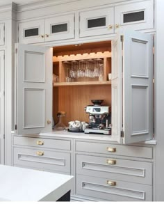 an open cabinet in a kitchen with wine glasses on the counter and other items inside